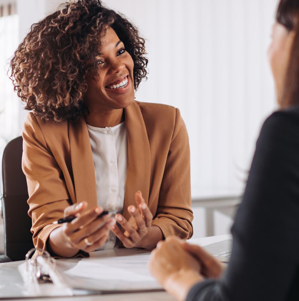 Travel agent smiling while assisting a client at an office desk.