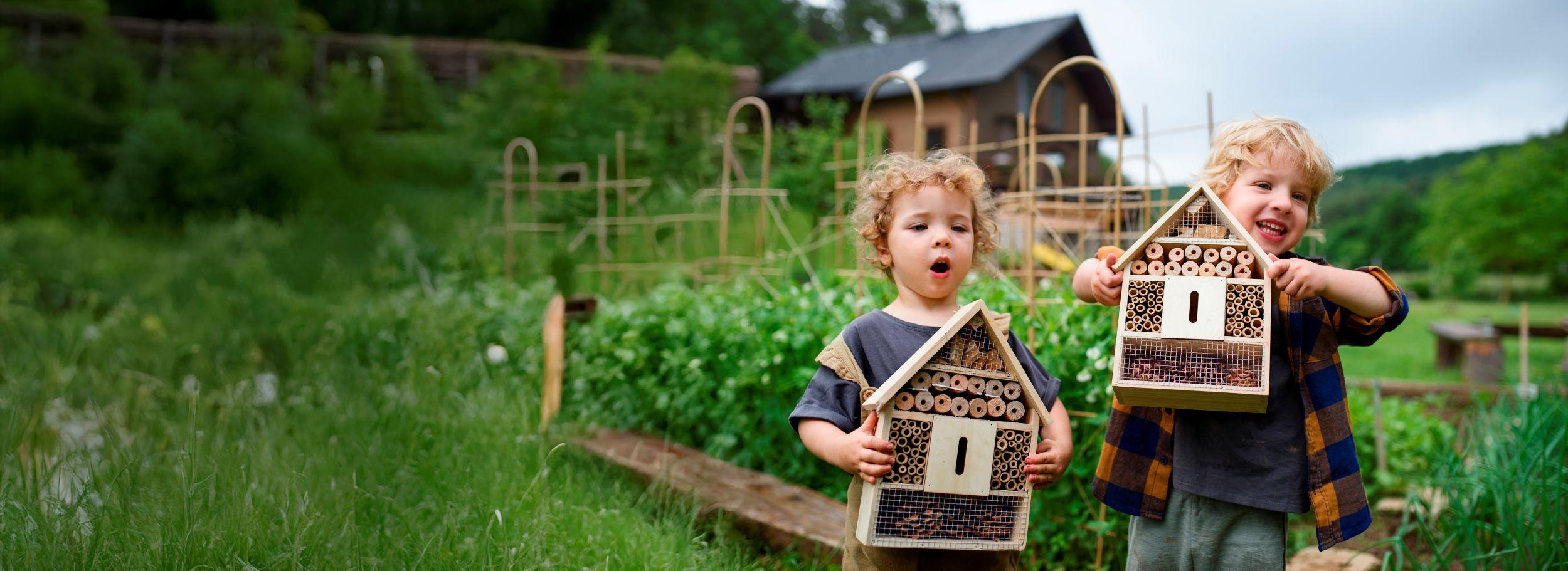 Deux enfants tenant des maisons à insectes en bois dans un jardin, faisant la promotion du tourisme durable.